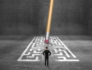 A person in a business suit stands facing a maze drawn on the ground. An oversized pencil with a large eraser appears to be erasing the maze, suggesting the removal of obstacles or finding solutions, much like strategies for employee retention. The background is dark and concrete-like.