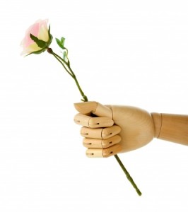 A wooden mannequin hand, symbolizing the delicate balance of career and life, gently holds a pink rose with green leaves against a pristine white background.