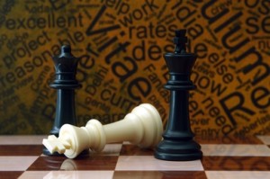 A chessboard with a white king piece lying on its side and a black king and queen standing upright. The background features a word cloud in yellow and black, resembling the highlights on a professional resume.