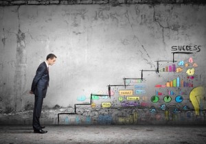 A man in a suit stands observing a concrete wall with colorful drawings depicting various business elements, growth charts, and performance goals leading to the word "SUCCESS" at the top. The wall appears weathered and cracked, contrasting with the vibrant illustrations.