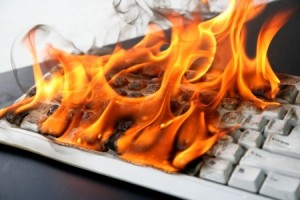 A keyboard engulfed in bright orange flames and thick smoke, with the keys melting from the intense heat. This image of technological destruction conveys a sense of urgent catastrophe.