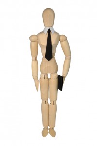A wooden mannequin, primed for an interview, is dressed in a collar and black tie. It stands upright, holding a black folder in its right hand, and poses against a plain white background.