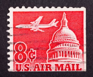 A vintage 8-cent U.S. Air Mail postage stamp showcases the U.S. Capitol dome with an airplane soaring above it, symbolizing the public sector in transit. The stamp is red and white with perforated edges, set against a black background.