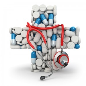 A red stethoscope rests on a cross made of various pills and capsules. The cross, formed by an arrangement of white and blue medication tablets against a white background, symbolizes medical and public health themes.