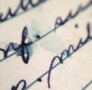A close-up of cursive writing on lined paper, with black ink slightly smudged and tinted by a light blue water stain. The letter's ink appears to have bled into the paper around the wet area, creating an abstract pattern.