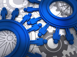 Illustration of blue human figures forming a network, connected like cogs in machinery with interlocking gears in the background. The image symbolizes HR innovation, teamwork, collaboration, and interconnected systems.