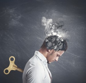 A man in a striped shirt is depicted with gears and smoke emerging from his head, symbolizing intense thought or mental pressure. A large wind-up key is inserted into his back, suggesting a mechanical or robotic element to his existence, emblematic of the grind of meaningless work.