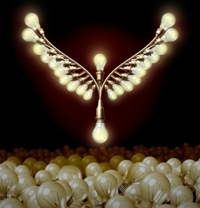 An artistic arrangement of illuminated light bulbs forms the shape of wings against a dark background, resembling a leader soaring above. Below the winged formation is a cluster of unlit light bulbs, appearing to lie on a surface.