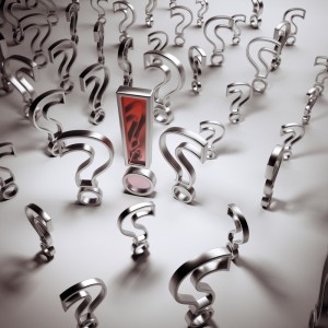 A red exclamation mark stands prominently among numerous metallic question marks on a reflective surface. The arrangement highlights the exclamation mark as a focal point, creating a striking contrast between the certainty it symbolizes and the surrounding uncertainty of asking why.