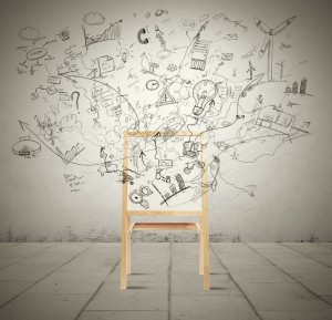 A wooden chair sits against a wall covered in sprawling black doodles and sketches. The imaginative drawings, possibly by a public policy analyst in their downtime, feature elements such as light bulbs, gears, buildings, and arrows, giving a dynamic and creative atmosphere. The floor is tiled in light gray.