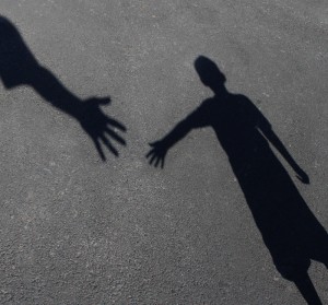 Shadows of two people on asphalt, with one shadow showing an outstretched arm and open hand reaching towards the other shadow, which also has an outstretched arm and open hand, suggesting an imminent connection or touch—much like the collaborative efforts fostered by USAID.