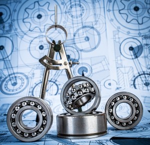 A set of ball bearings arranged on top of engineering blueprints, with a pair of metal calipers standing upright among them. The blueprints, stamped with a well-known brand logo, feature intricate mechanical designs and diagrams in blue and white colors.