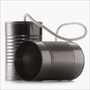 Two tin cans are connected by a piece of white string, forming a makeshift toy telephone—a nostalgic reminder that even the simplest tools can connect us. One can stands upright while the other lies on its side, revealing the interior ribbed texture. The image is set against a plain white background, much like how a job search requires clear focus.