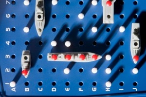 A close-up of a Battleship game board reveals an intense contest, reminiscent of international relations. Several ships with red pegs indicating hits are positioned on the blue, peg-filled grid. The grid is labeled with numbers 1-5 on the left and letters A-I on the bottom.