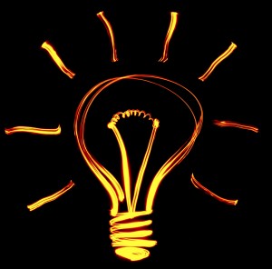 A glowing outline of a light bulb is drawn against a black background with bright orange light. Curved lines radiate outward from the top half of the bulb, symbolizing illumination and ideas—just like recruiters shining a light on hidden potential.