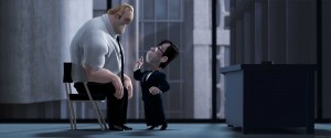 A large, muscular man in a white shirt and black tie sits on a small chair, looking down at a much shorter employee in a black suit who is standing and making a stern gesture with his hand. The setting appears to be a dimly lit office with a desk and large windows.
