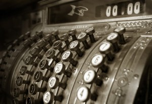 Sepia-toned close-up of an antique cash register with round buttons displaying numbers. The buttons are arranged in a circular fashion, and the display reads "00.00." An ornate design decorates the structure, highlighting its vintage style—taking you back to when a job behind the counter meant mastering such craftsmanship.