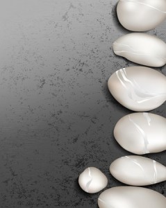 A team of smooth, white pebbles arranged in a gentle curve on the right side of a textured gray background. The pebbles vary in size and have subtle, milky-white streaks, creating a calming and minimalist composition.