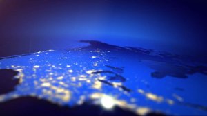 A view of Earth from space showing the North American continent illuminated by city lights at night. The image has a blue gradient background, with the landmass partially visible and areas of light representing populated regions.