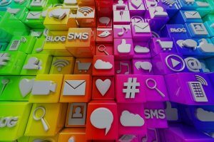 Colorful 3D blocks, each with a different social media or digital icon, including symbols for blogs, SMS, shopping carts, hearts, music notes, clouds, video players, and magnifying glasses. The blocks are arranged in a gradient from green to pink and purple.