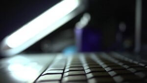 Close-up image of a laptop keyboard, with the backlight of the monitor creating an illuminated effect. The background is blurred, featuring indistinct shapes and a soft mix of dark and light colors, evoking a focused and serene atmosphere.