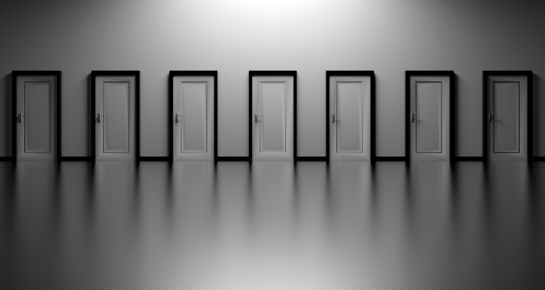 A monochromatic image showing a row of seven closed doors evenly spaced along a reflective wall. The doors are identical in style and color, creating a symmetrical and minimalist visual effect. The lighting emphasizes shadows and highlights the reflection on the floor.