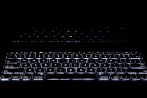 A close-up view of an illuminated keyboard in a dark environment. The keys are backlit with white light, creating a glowing effect that highlights the letters and symbols. The background is almost entirely black, emphasizing the bright keys—perfect for those late-night information governance tasks.