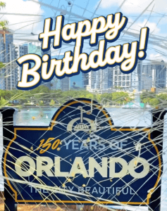 A festive sign reads "Happy Birthday! 150 Years of Orlando, Truly Beautiful" with a city skyline and lake in the background, overlaid with white celebratory streamers.