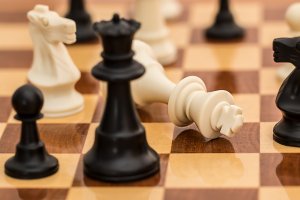 Close-up of a chessboard with a focus on the white king piece laying on its side, surrounded by other chess pieces in various positions. The pieces include white and black knights, pawns, and queens. The image suggests strategic decisions leading to the concluded game, with the white side defeated.