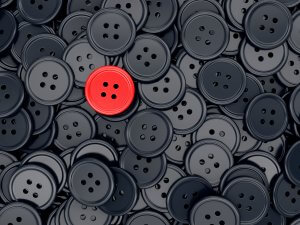 A collection of black four-hole buttons with one prominent red four-hole button in the center, standing out like successful people among the crowd.