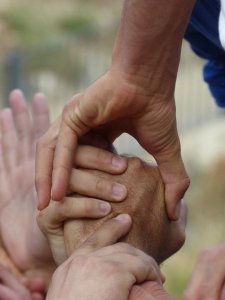 Several hands are clasped together in a supportive gesture, creating a chain of unity. The image focuses on the connection of the hands, symbolizing teamwork, cooperation, and mutual support among employers. The background is blurred, keeping the attention on the hands.