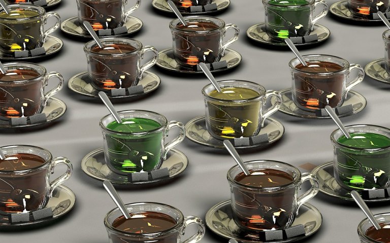 Rows of glass teacups on saucers, each filled with a different-colored liquid ranging from brown to green. A metallic spoon rests in every cup, and a tea bag with a yellow tag is infusing in the liquid. This vibrant display adds a touch of worksite wellness to the simple light gray background.
