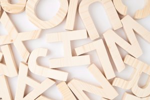 A scattered collection of light wooden alphabet letters in various sizes lies against a plain white background, reminiscent of crafting a cover letter. The letters are made from smooth, light-toned wood, with each letter featuring a distinct, clean-cut shape.