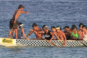 A group of people are paddling a dragon boat on the water. The team is focused and coordinated, with one person standing at the front, presumably giving directions. Each member is actively rowing, showcasing how character matters in achieving their goals as they glide in a boat featuring a distinctive dragon scale pattern.