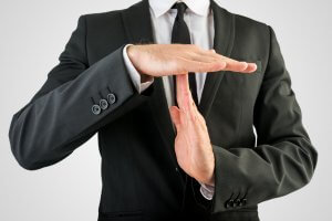 A person in a black suit and black tie is making a time-out gesture with their hands, forming a 'T' shape in front of their chest against a neutral background, likely signaling the need for a break during a busy work day.
