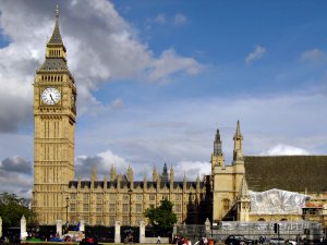 Big Ben and the Palace of Westminster in London on a partly cloudy day. The clock tower is prominent on the left while the Gothic architecture of the parliamentary buildings extends to the right. Pedestrians and tourists can be seen near the foreground.