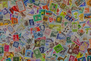 A colorful assortment of postage stamps from various countries and time periods, scattered randomly. These postage stamps feature diverse designs, including historical figures, landmarks, animals, and cultural symbols, showcasing a rich variety of artwork and themes.
