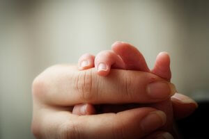 Close-up of an adult hand gently holding a newborn's delicate fingers, much like a moment captured on a postage stamp, emphasizing the bond and tenderness between them. The background is softly blurred, drawing focus to the intimate connection.