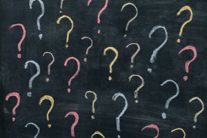 A chalkboard with multiple question marks drawn in various colors, including pink, yellow, white, and light blue. The chalkboard serves as a dark backdrop, making the colorful questions stand out prominently.