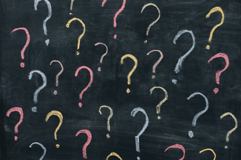 A chalkboard with multiple question marks drawn in various colors, including pink, yellow, white, and light blue. The chalkboard serves as a dark backdrop, making the colorful questions stand out prominently.