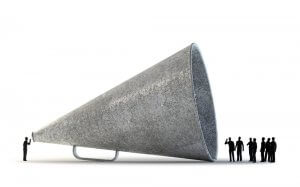 A large, metallic megaphone lies on its side. A small figure at the narrow end speaks into it, demonstrating soft skills, while a group of small figures stands and listens at the wide end. The scene is set against a plain white background.