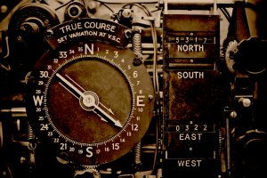 A close-up of a vintage navigational instrument with a large compass dial marked with cardinal directions (N, E, S, W) and bearings. Featuring indicators and scales for setting true course and variation adjustments, this aged mechanical device exemplifies leadership in maritime navigation.
