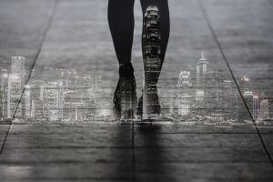 A double exposure image shows a person's silhouetted legs and feet walking on pavement, superimposed with a bright, illuminated city skyline at night. This surreal and artistic visual effect captures the essence of urban life and movement, symbolizing the endless leadership opportunities in an ever-evolving cityscape.