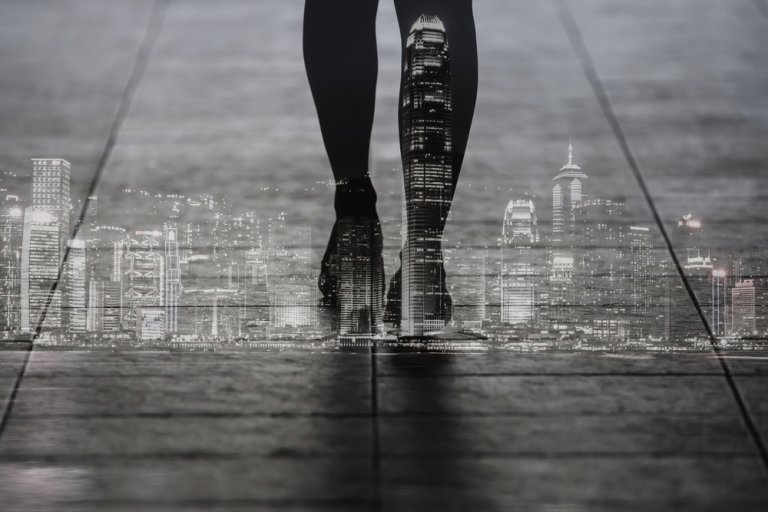 A double exposure image shows a person's silhouetted legs and feet walking on pavement, superimposed with a bright, illuminated city skyline at night. This surreal and artistic visual effect captures the essence of urban life and movement, symbolizing the endless leadership opportunities in an ever-evolving cityscape.