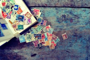 A collection of brightly colored postage stamps is spread out on a weathered wooden surface. Some stamps are organized in an open stamp album on the left, while others are scattered randomly across the blue and brown textured wood, reflecting a sense of self-esteem through their vibrant display.
