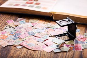 A collection of vintage postage stamps spread out on a wooden surface alongside a magnifying glass, with a partially visible open stamp album in the background. The stamps, in various colors and designs, evoke a sense of self-esteem for any keen collector.