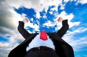 A person in a suit with a red tie raises their arms triumphantly towards a sky filled with dynamic clouds. The perspective is from a low angle, making the recently promoted figure appear powerful and victorious against the vibrant backdrop.