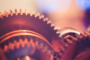 Close-up of interlocking gears with a warm, orange tint. The image focuses on the teeth of the gears, highlighting their precision and detail, much like a well-coordinated team. The background is softly blurred, creating a contrast that draws attention to the mechanical elements.