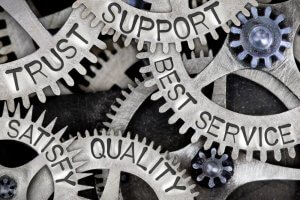 Close-up image of interlocking metal gears with words inscribed on them, such as "Trust," "Support," "Best Service," "Satisfy," and "Quality." These gears symbolize the interconnected elements of successful teamwork, support, and customer service, representing concepts of reliability and excellence.