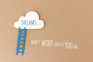 A white cloud with the word "DREAMS..." in blue text is connected to a blue ladder on a brown background. Below the ladder, the text reads, "DON'T WORK UNLESS YOU DO," encouraging you to overcome fear and take action.